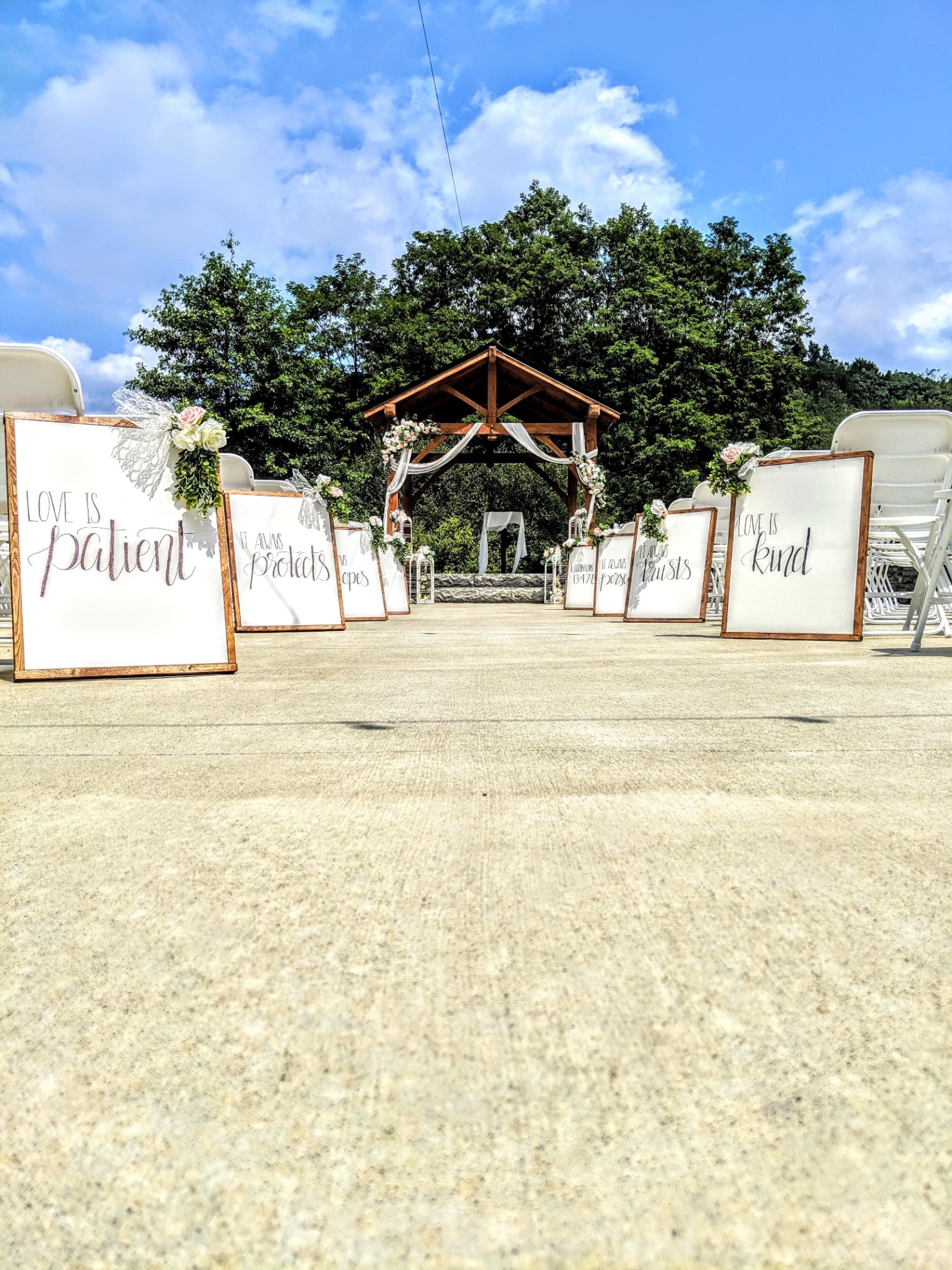 Ceremony aisle with lettered signs Outdoor ceremony aisle lined with hand-lettered Love is Patient signs leading to the timber pavilion