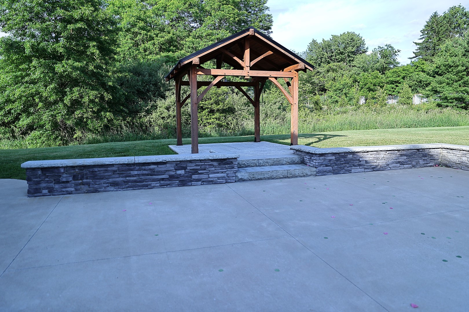Ceremony pavilion Timber-framed ceremony pavilion beside a stacked stone seating wall and stamped concrete patio