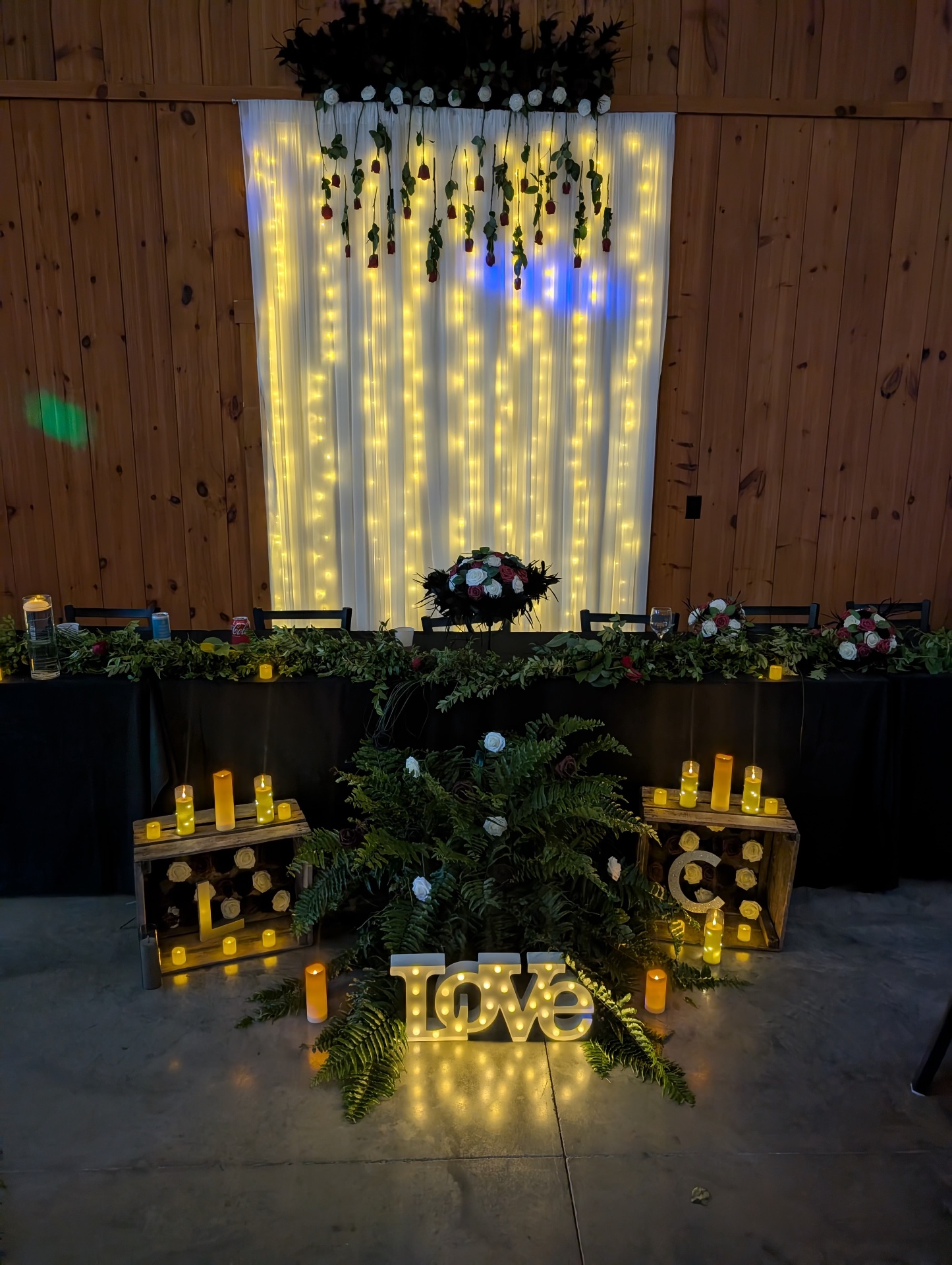Evening head table backdrop Head table backdrop of string lights and hanging roses with a lit LOVE sign and candles