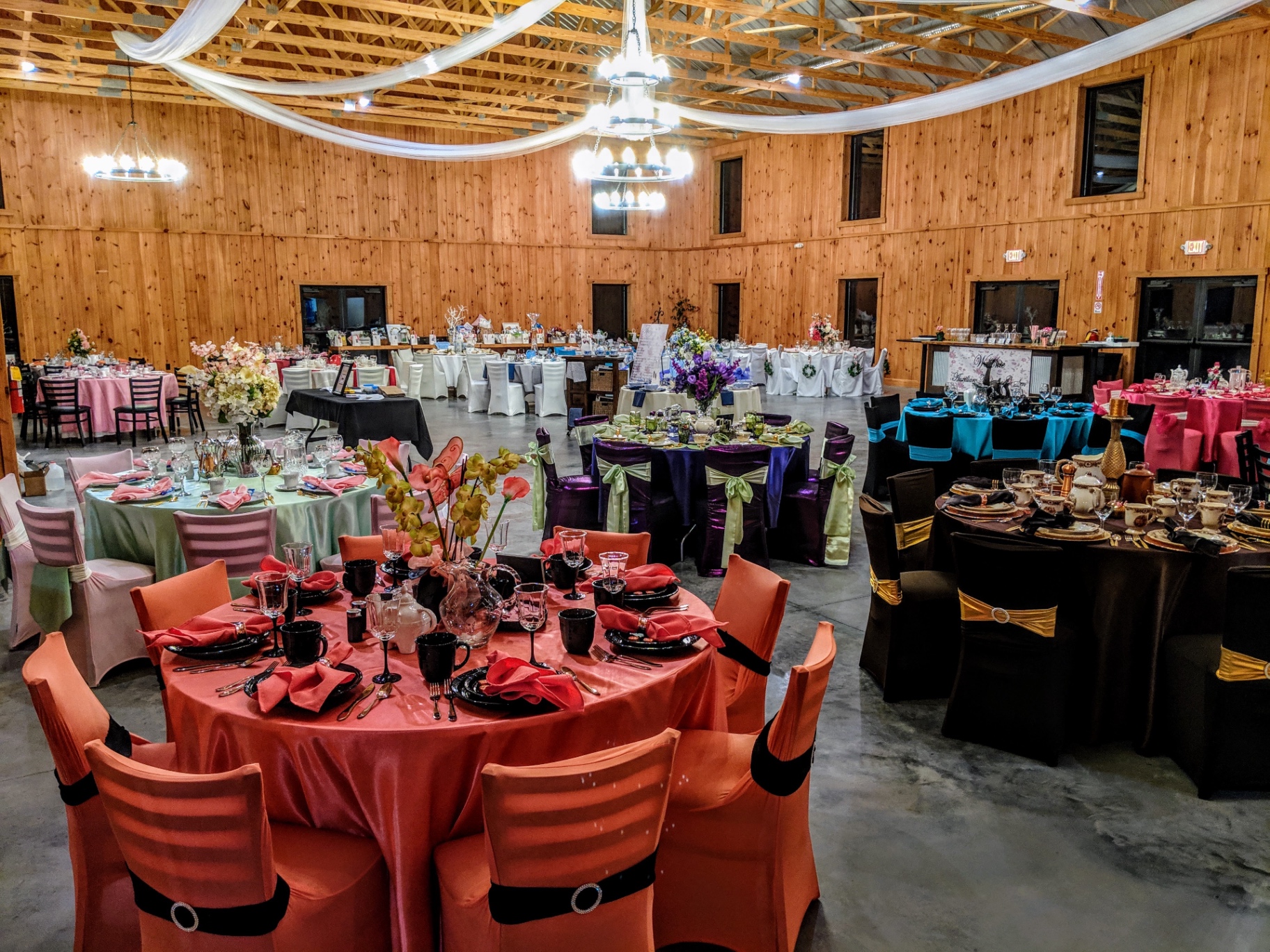 Reception hall fully set Full barn reception hall set with round tables in varied linen colors under chandeliers and white draping