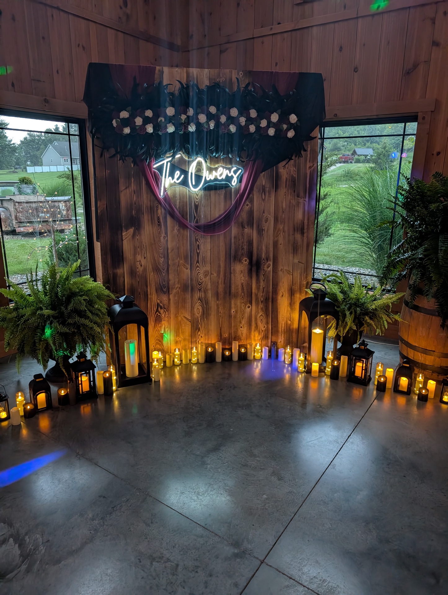 Neon sign photo backdrop Custom neon last-name sign on a wood plank backdrop surrounded by lanterns, candles and ferns